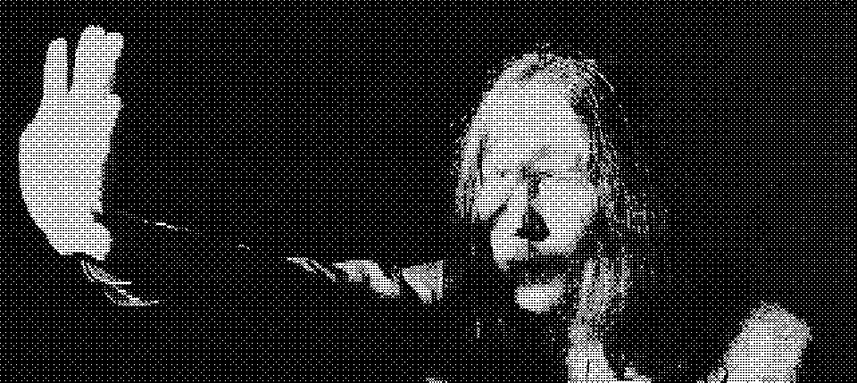 A figure with long hair holding a hand up toward the camera, in harsh black and white